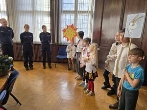 Kolędujące dzieci stoją w sali przed przedstawicielami Policji