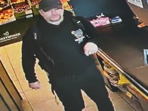 Mężczyzna w czarnych dresach i czarną czapką bejsbolówka robi w sklepie zakupy.