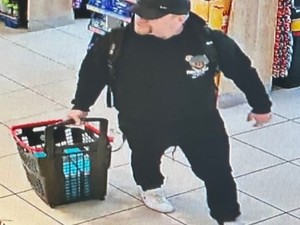 Mężczyzna w czarnych dresach i czarną czapką bejsbolówką robi w sklepie zakupy.