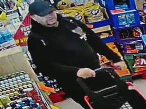 Mężczyzna w czarnych dresach i czarną czapką bejsbolówką robi w sklepie zakupy.