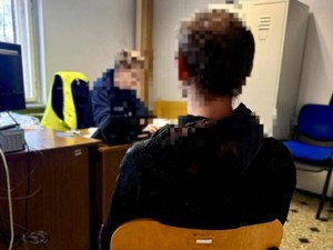 Przy biurku siedzi nieumundurowany policjant i przesłuchuje zatrzymanego