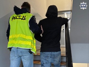 Policjant prowadzi zatrzymanego po schodach
