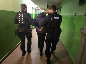 Dwóch policjantów prowadzi zatrzymanego korytarzem.