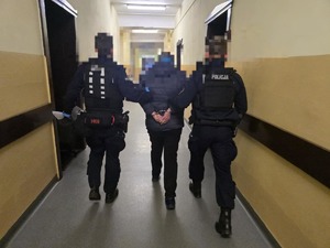 Policjanci prowadzą zatrzymanego korytarzem
.