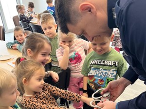 Dzielnicowy podczas spotkania a dziećmi pokazuje im, jak wyglądają kajdanki