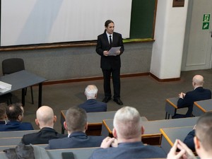 Na auli wykładowca stoi na środku sali prowadząc zajęcia