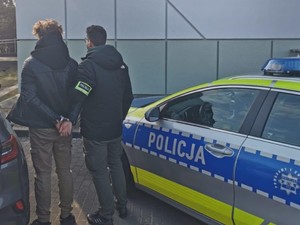 Koło radiowozu stoi podejrzany w cywilnym ubraniu