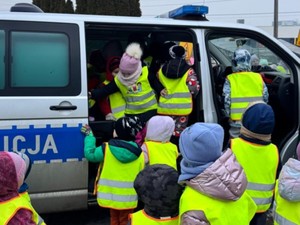 Dzieci w kamizelkach odblaskowych oglądają policyjny radiowóz