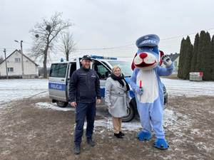 Na zdjęciu Sznupek, policjant i przedstawicielka szkoły, pozują do zdjęcia.