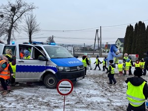 Grupa dzieci biega wokół radiowozu i Sznupka