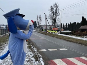 Sznupek stoi przy przejściu dla pieszych. Z dala idzie grupa dzieci chodnikiem