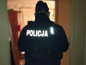 Policjant umundurowany stojący w drzwiach mieszkania.