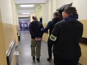 Policjanci prowadza zatrzymanego korytarzem,