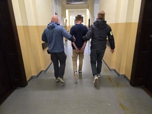 Policjanci prowadza zatrzymanego korytarzem