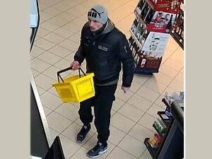 Mężczyzna w szarej czapce z napisem PUMA i kurtce. W ręku trzyma koszyk na zakupy.