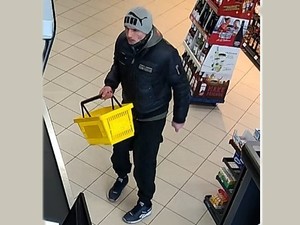 Mężczyzna w szarej czapce z napisem PUMA i kurtce. W ręku trzyma koszyk na zakupy.