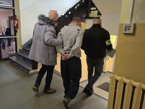 Zatrzymanego mężczyznę w kajdankach prowadzą policjanci