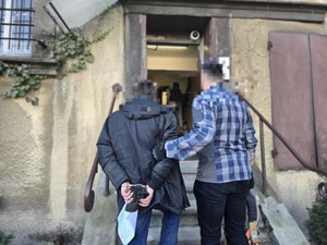 Na zdjęciu policjant prowadzi po schodach poszukiwanego w kajdankach