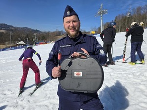 Policjant z walizką na stoku - w tle uczestnicy warsztatów.