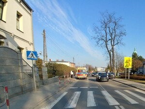 Na zdjęciu stoi na ulicy karetka pogotowia, po drugiej stronie drogi pojazd osobowy