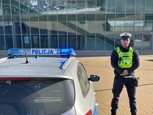 Umundurowany policjant stoi obok radiowozu