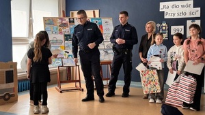 wręczanie nagród podczas gali finałowej, w tle widzimy dzieci i wręczających nagrody policjantów.
