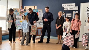 wręczanie nagród podczas gali finałowej, w tle widzimy dzieci i wręczających nagrody policjantów.