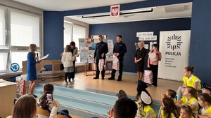 wręczanie nagród podczas gali finałowej, w tle widzimy dzieci i wręczających nagrody policjantów.