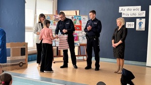 wręczanie nagród podczas gali finałowej, w tle widzimy dzieci i wręczających nagrody policjantów.