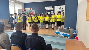 na zdjęciu zobaczymy śpiewające dzieci na scenie, każde dziecko jest ubrane w kamizelkę odblaskową oraz czapkę policyjną.