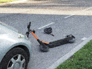 Zdjęcie leżącej na jezdni hulajnogi elektrycznej przed pojazdem.