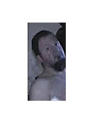 Zdjęcie przedstawia zapis monitoringu: mężczyznę z wyglądu około 35-40 lat, posiada zarost w postaci brody, ma ciemne włosy