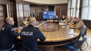 Na zdjęciu widzimy rozmawiących przy stole komendantów z nowo przyjętymi policjantami. Zdjęcie zrobione za plecami.