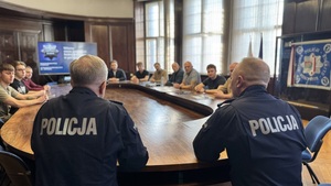 Na zdjęciu widzimy rozmawiących przy stole komendantów z nowo przyjętymi policjantami. Zdjęcie zrobione za plecami.