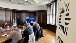 Na zdjęciu widzimy rozmawiących przy stole komendantów z nowo przyjętymi policjantami. Zdjęcie zrobione koło banneru gliwickiej policji.