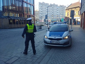Policjant stoi na jezdni obok oznakowanego radiowozu
