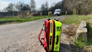 na pierwszym planie widzimy specjalistyczny plecak ratunkowy straży pożarnej w tle na polanie pootwierany helikopter ratunkowy.