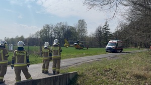 widzimy startujący helikopter ratunkowy, a pod nim karetkę pogotowia i obserwujących to wszystko strażaków.