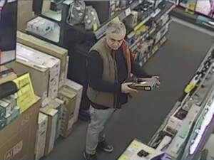 Na zdjęciu starszy mężczyzna stoi w sklepie ze sprzętem AGD pomiędzy półkami, trzymając w rękach jakiś przedmiot.