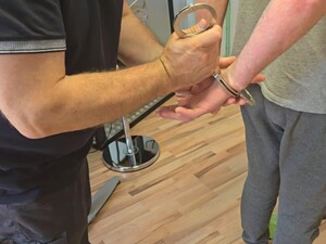 Policjant nieumundurowany zakłada zatrzymanemu kajdanki.