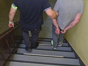 Policjant sprowadza zatrzymanego po schodach.