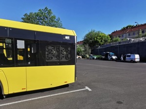 Na dużym placu stoi autobus oraz pojazdy służb
