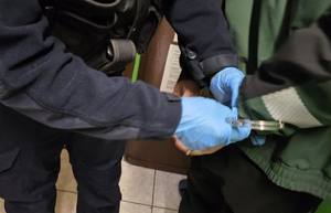 Na zdjęciu policjant zapina kajdanki osobie poszukiwanej.