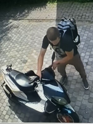 Na zdjęciu młody chłopak w ciemnej koszulce i długich spodniach, prowadzący motorower.