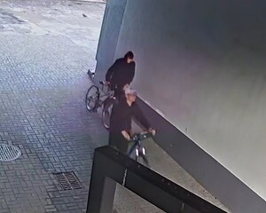 Dwóch mężczyzn prowadzący rowery,    koło budynku. W tym jeden w czapce bejsbolowej.