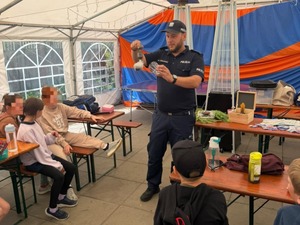 Policjant umundurowany prowadzi dla dzieci z półkolonii zajęcia pod namiotem