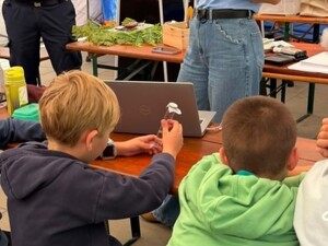 Dzieci siedząc przy ławce oglądają probówkę z materiałem poglądowym