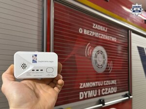 Czujnik tlenku węgla trzymany w ręku, na tle pojazdu straży pożarnej