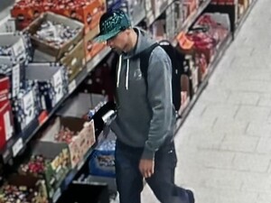 Mężczyzna w czapce bejsbolowej w sklepie samoobsługowym ciągnie koszyk.
