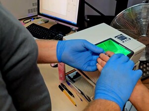 Technik kryminalistyki pobiera odciski palców zatrzymanemu